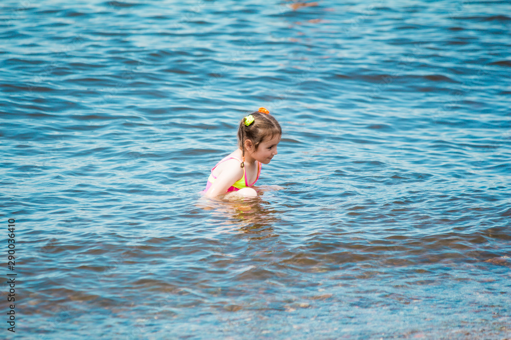 Little girl in a swimsuit bathing in the sea in summer, making a splash and running in water