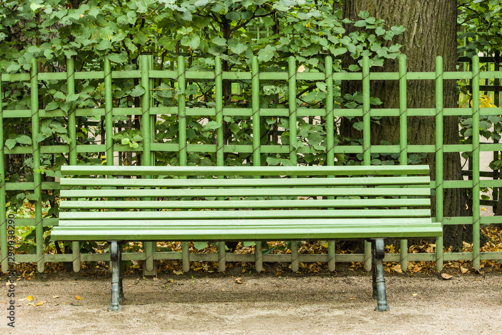 green wooden street bench on a background of green metal fence with plants