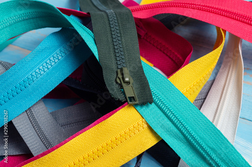 Pack lot of colorful plastic and metal zippers stripes with sliders pattern for handmade sewing tailoring on the blue painted wooden background close up selective focus