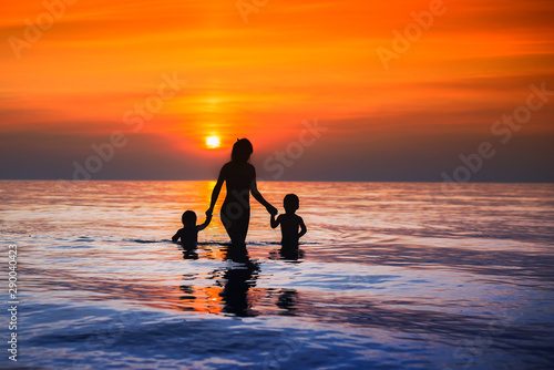 Beautiful at sunset silhouettes of mothers with children going from the sea to the shore  the concept of communication with children mom lonely mom loves her children
