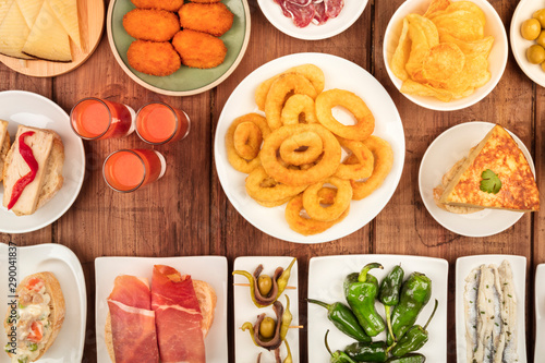 Spanish tapas, an overhead photo of a variety of snacks. Gazpacho, squid rings, tortilla, jamon, cheese etc, shot from the top on a dark rustic wooden background