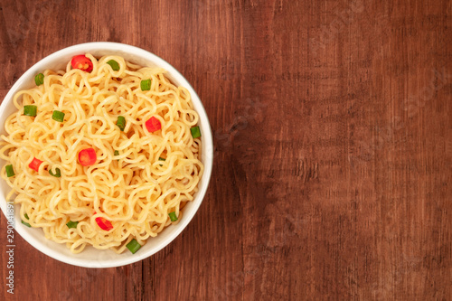 A bowl of noodles, shot from the top on a dark rustic wooden background with a place for text