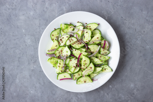 Fresh cucumber salad with flax seeds on gray stone background. Top view.