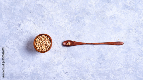 pine nut in a wooden bowl whith wooden spoon on a blue and white background top view