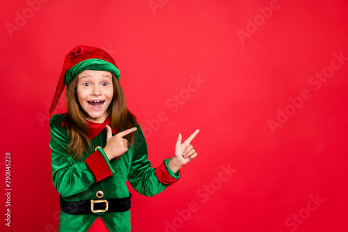 Portrait of impressed funky elf in hat cap showing ads with her index fingers screaming wow omg see magic wearing green costume isolated over red background