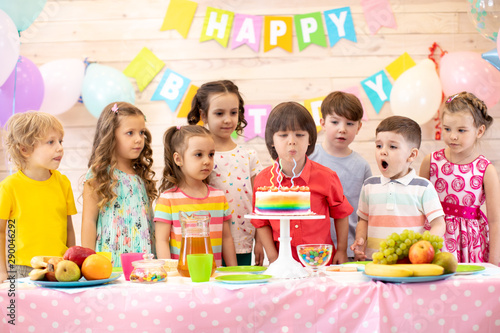 Child boy together with friends blowing the candles of its cake of birthday. Group of kids on party in daycare centre