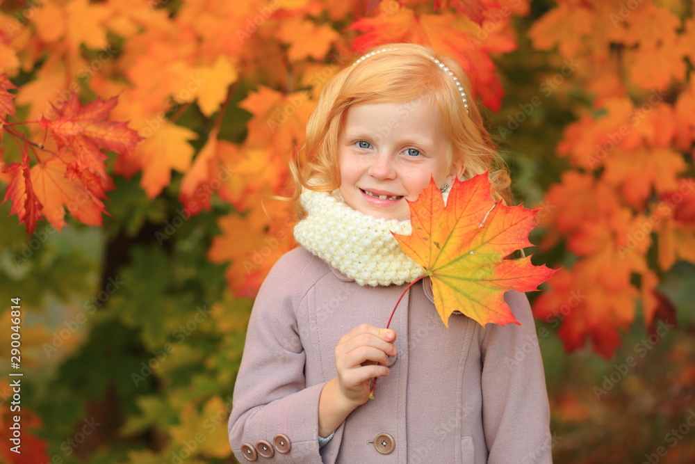 A girl with red hair plays in the autumn park. Autumn palette. Portrait of ginger child A girl with red hair plays in the autumn park. Autumn palette. Portrait of ginger child