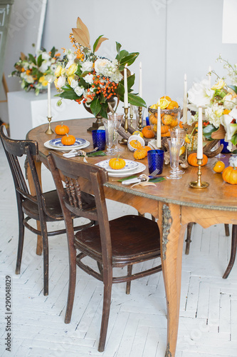 Luxurious elegant wedding decor in autumn style. Wooden vintage table and chairs setting with ceramic plates and silver cutlery. Fresh flowers in a vase  orange pumpkins  deer horns and candles.