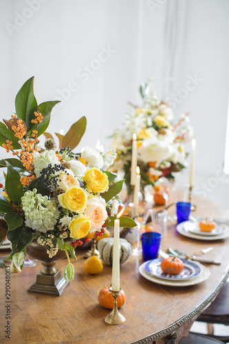 Luxurious elegant wedding decor in autumn style. Wooden vintage table setting with ceramic plates and silver cutlery. Fresh flowers in a vase, orange pumpkins, deer horns and candles. Romantic dinner.