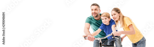 panoramic shot of smiling parents teaching son to ride bike isolated on white