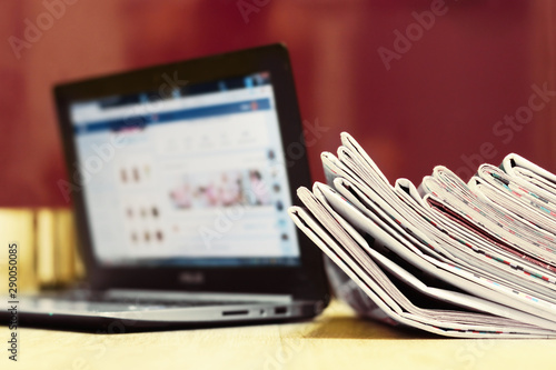 Stack of Newspapers next to Open Laptop. News on Paper Pages or on Screen of Computer. Media and Press Concept                      