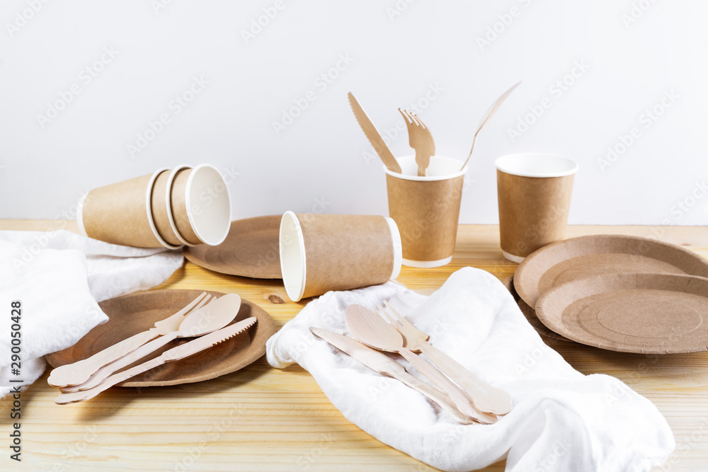 Brown paper cups, plates, wooden cutlery, linen napkins on wooden background. Recycling concept. Brown paper cups, plates, wooden cutlery, linen napkins on wooden background. Recycling concept.