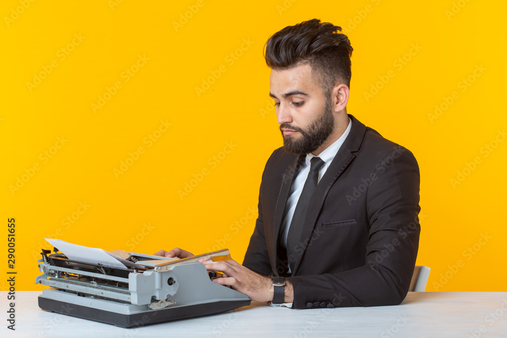 Young handsome male businessman in formal clothes typing text on a typewriter posing on a yellow background. Place for advertising. Business concept.