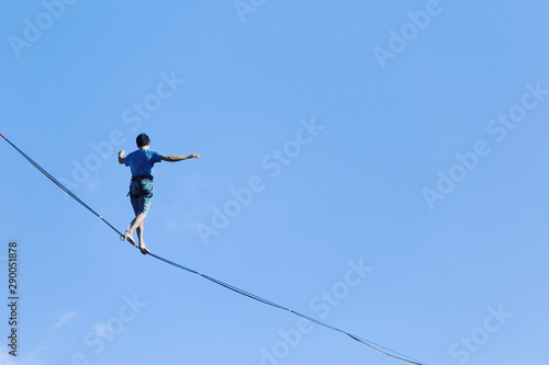 A man is walking along a stretched sling. Highline in the mountains. Man catches balance. Performance of a tightrope walker in nature. Highliner on the background of the mountains.