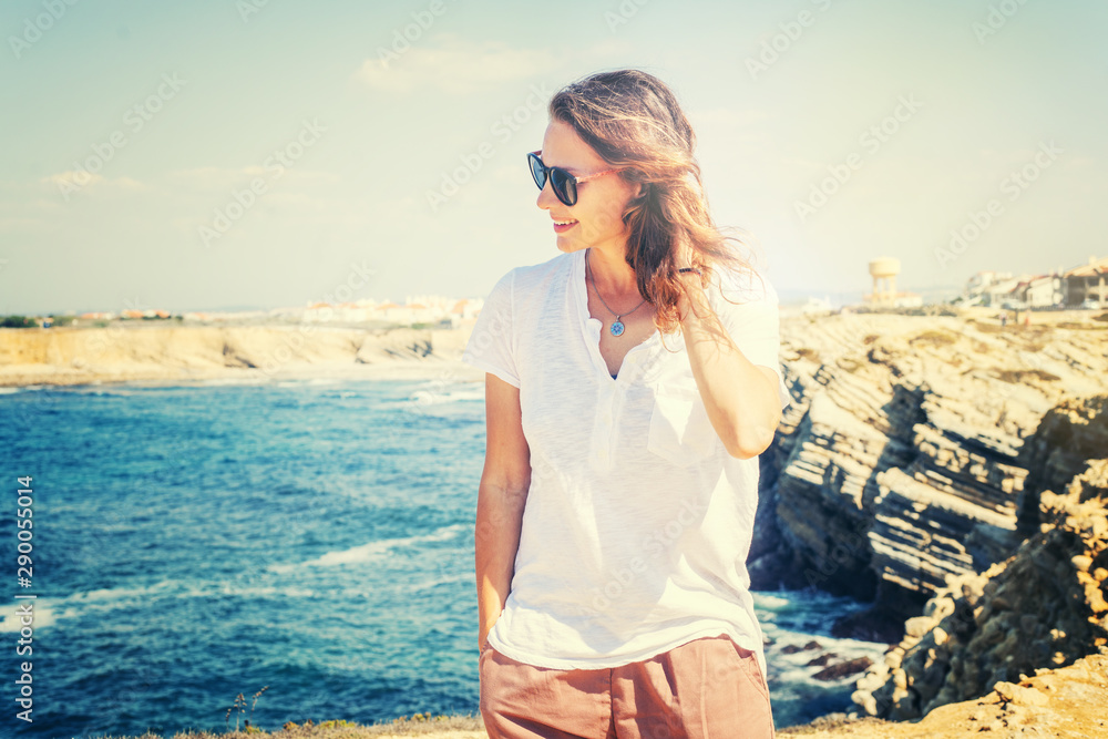 Beautiful young woman with a happy smile in a white T-shirt on the ocean in Portugal, travel and relax Beautiful young woman with a happy smile in a white T-shirt on the ocean in Portugal, travel and relax