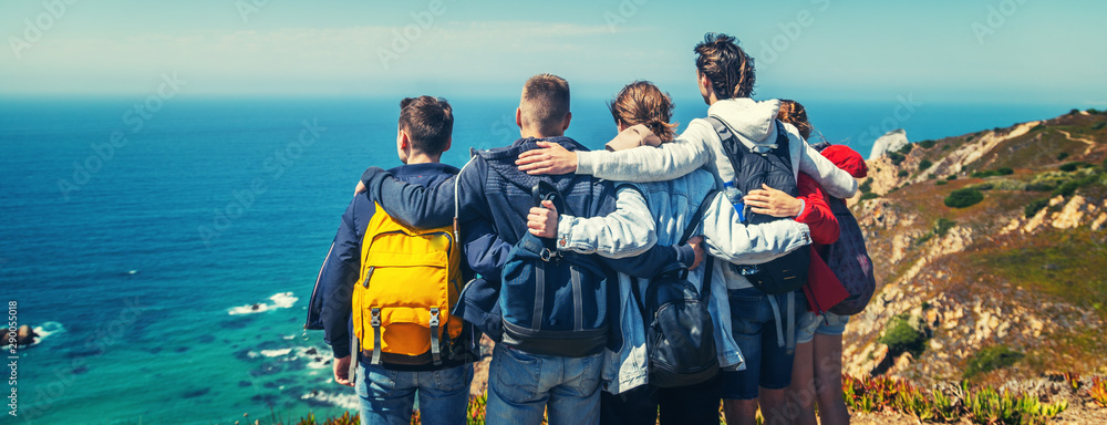 A company of young happy friends travels in Portugal, stands on the shore of the Atlantic Ocean and hugs, travell together, community friendship vacation - obrazy, fototapety, plakaty 