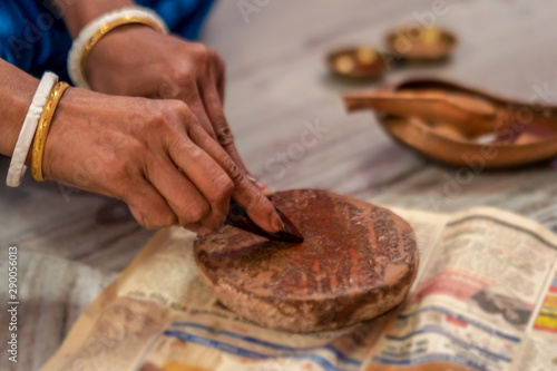 Person Rubbing Sandalwood. Indian woman rubbing sandalwood or chandan on a stone for puja or pooja preparation. Background image for hindu culture, tradition or Durga Puja with copy space.