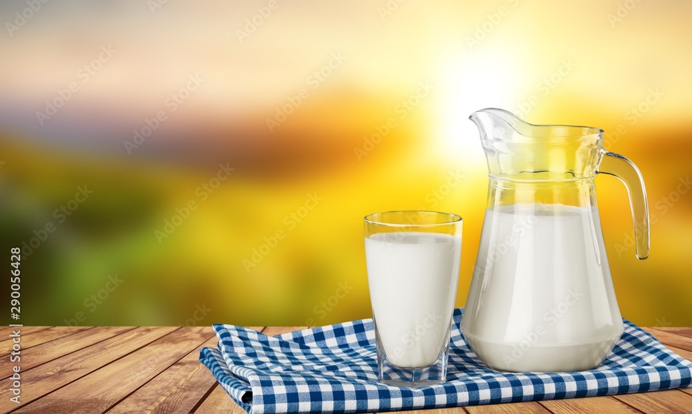 A glass of milk and a milk jug on plaid tablecloth A glass of milk and a milk jug on plaid tablecloth