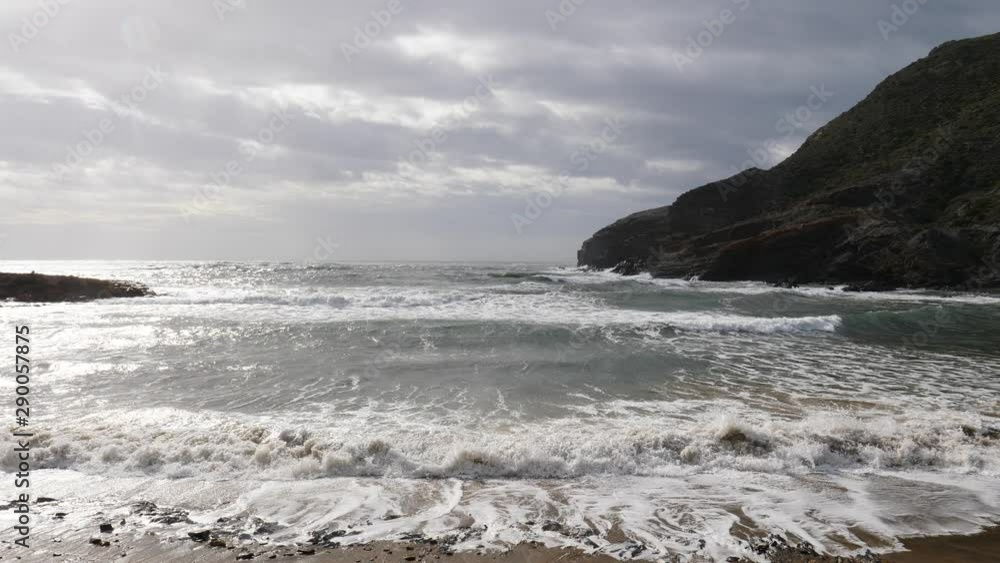 Spanish beach sea waves at cloudy rainy weather. Cala Reona in Cabo de Palos. Mediterranean Sea landscape, coast in Murcia region. Tourist site. Slow motion Spanish beach sea waves at cloudy rainy weather. Cala Reona in Cabo de Palos. Mediterranean Sea landscape, coast in Murcia region. Tourist site. Slow motion