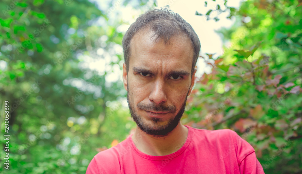 A portrait of a handsome man with beard against the background of green trees in the park. A portrait of a handsome man with beard against the background of green trees in the park.