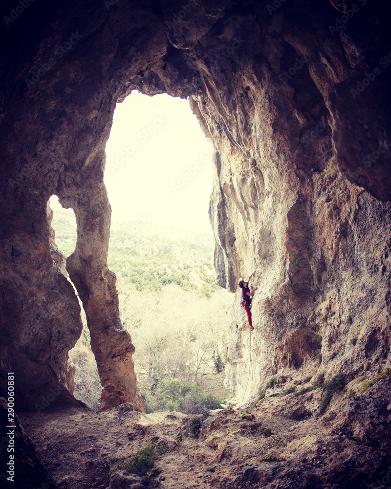 A man climbs the rock against of a mountain landscape. The athlete trains on a natural relief. Climbing in Turkey. Rock in the form of an arch. Cave. The climber overcomes a difficult route.