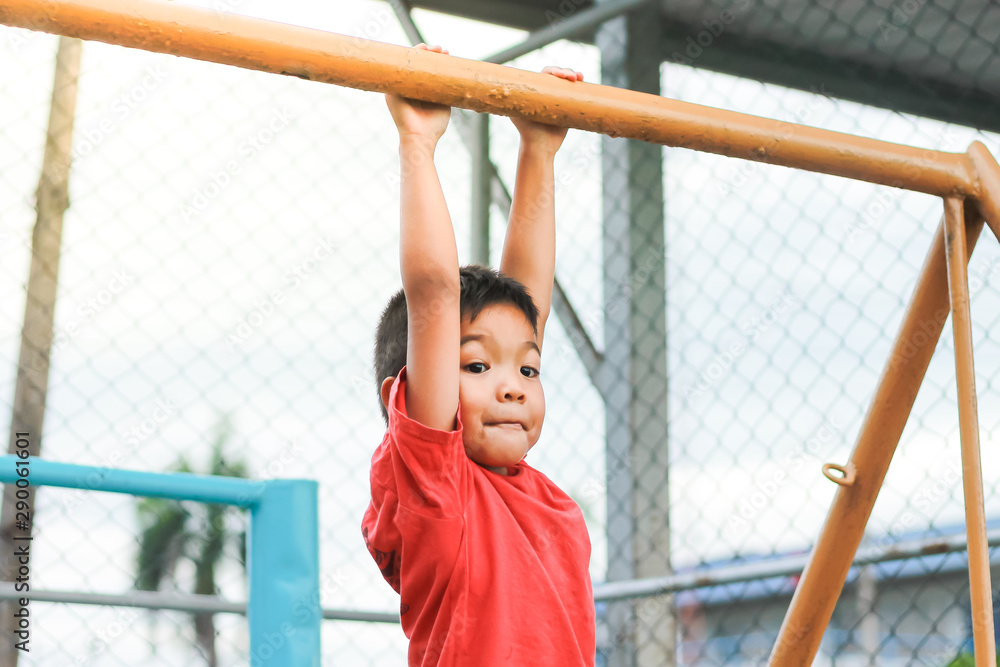 Obraz premium Kid exercise for health and sport concept. Happy Asian child boy playing and hanging from a steel bar at the playground. 5 years old.