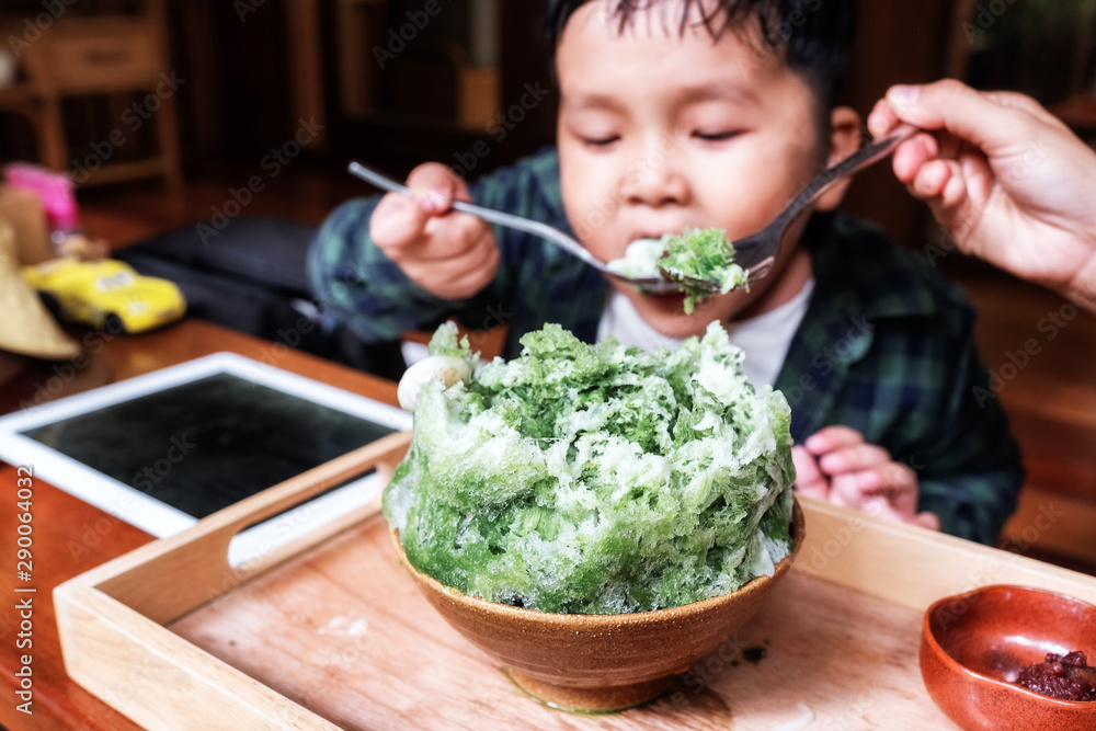Matcha kakigori or bingsu on wooden table with little boy eating background.