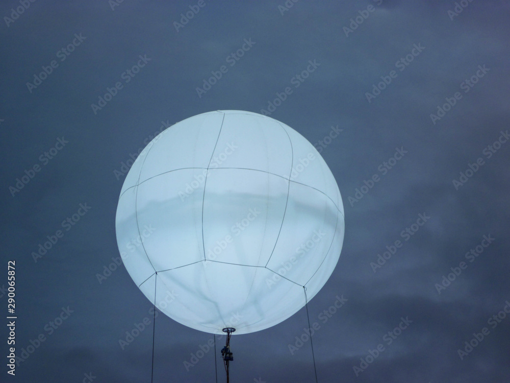 A backlit balloon is launched on ropes into the dark night sky. A backlit balloon is launched on ropes into the dark night sky.