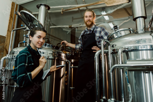 Women with clipboard working at brewery or beer plant. Brewery worker opening a lid of a beer cask at a craft beer brewery. Small business concept.