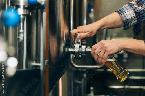 Photographie Brewer filling beer in glass from tank at brewery