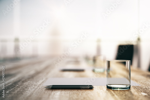 Foto Close up of blurry wooden conference table with glass, pens and blank sheet in the morning