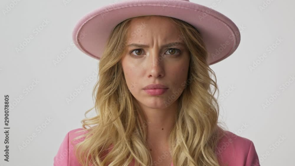 Close up view of cheerful young blonde woman in pink jacket and hat smiling and laughing while looking at the camera over gray background isolated Close up view of cheerful young blonde woman in pink jacket and hat smiling and laughing while looking at the camera over gray background isolated