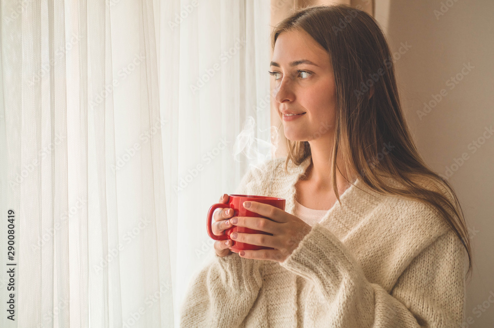 Woman with cup of hot drink by the window. Looking at window and drink tea. Good morning with tea