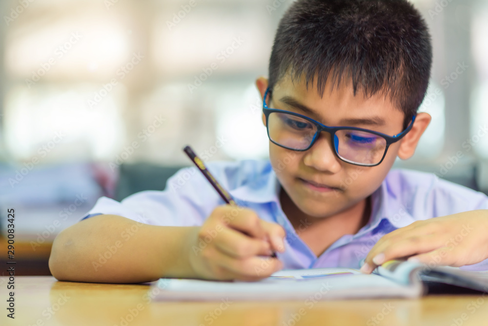 Asian elementary school boy in a white school uniform and wearing glasses, is studying in the classroom. - obrazy, fototapety, plakaty 