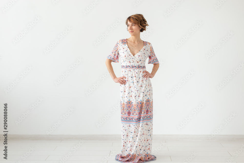 Charming young woman posing on a white background in a long light bright summer dress. The concept of exquisite women's clothing. Charming young woman posing on a white background in a long light bright summer dress. The concept of exquisite women's clothing.