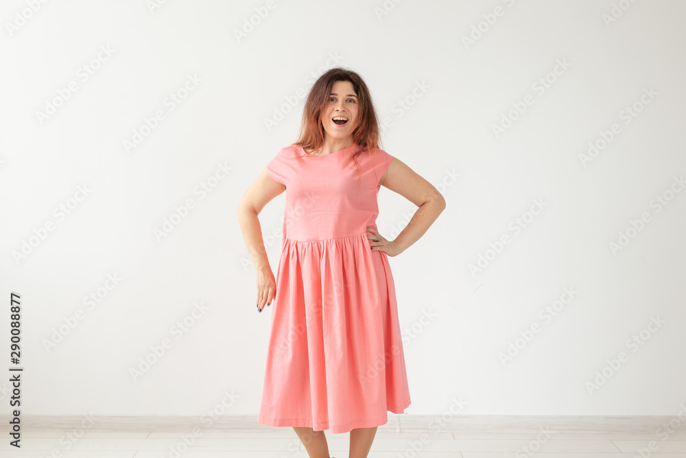Beautiful young cheerful woman in a long peach dress posing on a white wall. Concept of stylish young woman. Copy space Beautiful young cheerful woman in a long peach dress posing on a white wall. Concept of stylish young woman. Copy space