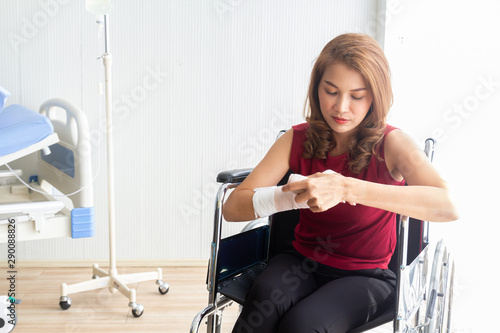 A female Asian patient suffered an accident with her arm broken, causing her to sit in a wheelchair. Her doing wrapping the bandage on the splint by herself.
