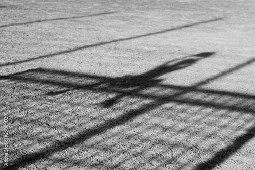 Schattenwurf eines Fußballtorwarts, der auf dem Tor sitzt und den Fussball mit erhobenen Armen gefangen hat auf einem Aschenplatz mit Schatten des Tores und der Umzäunung des Fussballplatzes