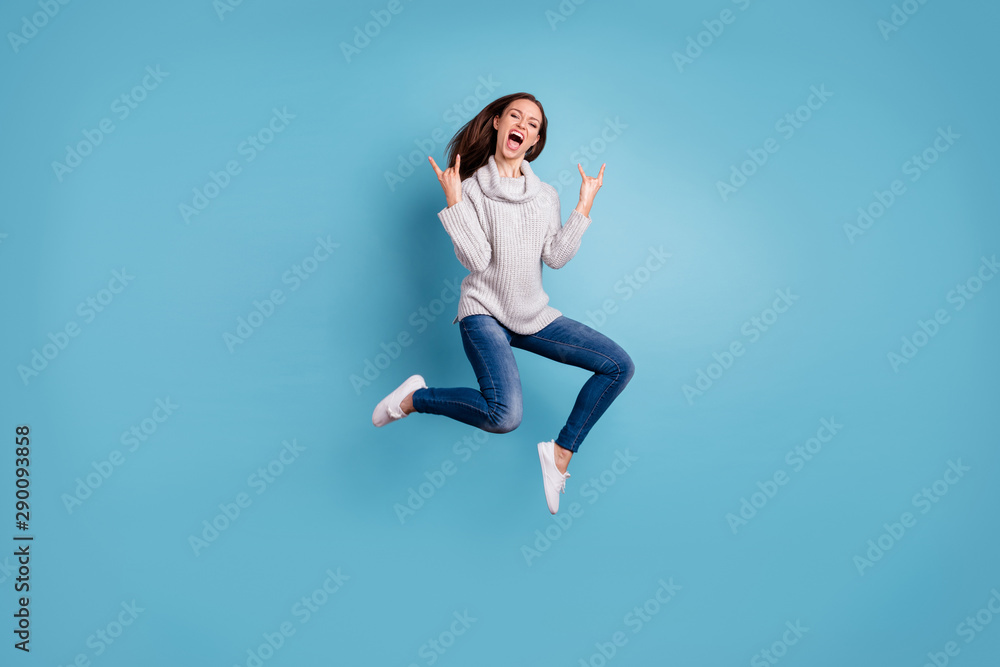 Full length photo of cheerful content youth jump show horns signs jump feel rejoice have weekend party wear white pullover denim jeans sneakers isolated over blue color background