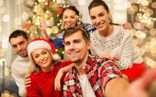 celebration and holidays concept - happy friends with glasses celebrating christmas at home party and taking selfie