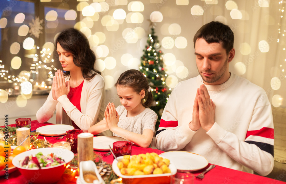 holidays, family and celebration concept - happy mother, father and little daughter having christmas dinner and praying before meal at home
