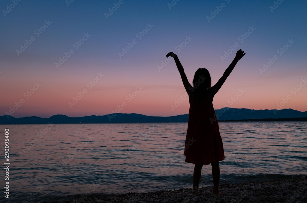 Young girl dancing on pebble beach after sunset