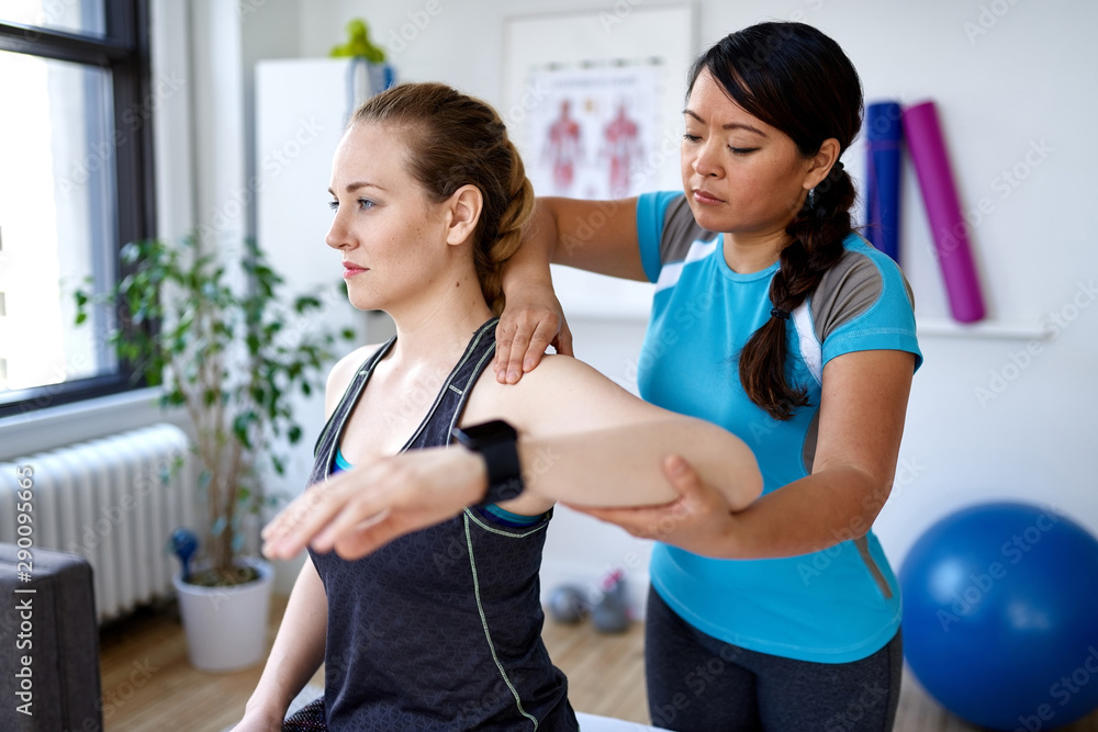 © AYAimages - Chinese woman physiotherapy professional giving a treatment to an attractive blond client in a bright medical office