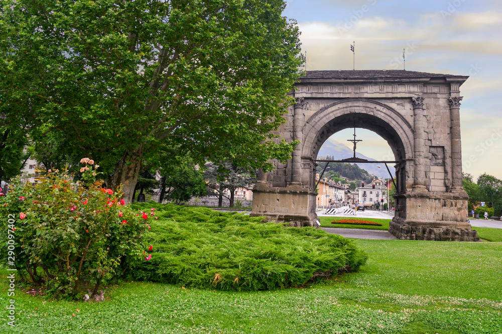 Obraz premium View of the Arch of Augustus, a monument erected in 25 BC on the occasion of the Roman victory over the Salassi, from a public park in summer, Aosta, Aosta Valley, Italy