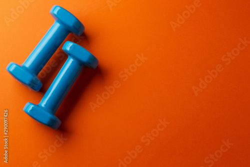Two blue dumbbells for a girl on an orange background, top view