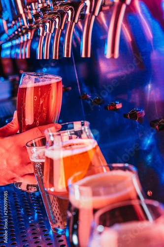 Hand of bartender pouring a large lager beer in tap. Bright and modern neon light, males hands. Pouring beer for client. Side view of young bartender pouring beer while standing at the bar counter. photo