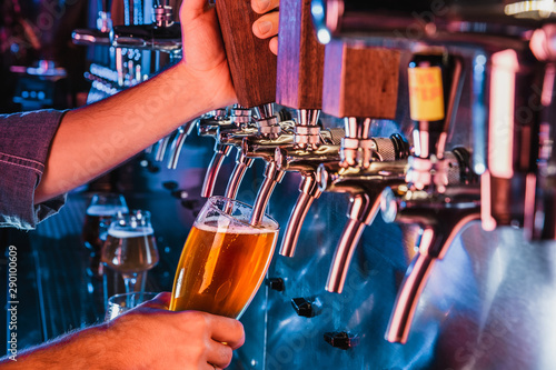 Hand of bartender pouring a large lager beer in tap. Bright and modern neon light  males hands. Pouring beer for client. Side view of young bartender pouring beer while standing at the bar counter.