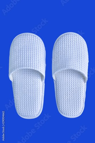 White, clean hotel slippers on a blue background