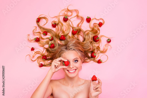 Vertical side profile top above high angle view photo beautiful toothy she her lady lying down among strawberries long curly wavy hair yummy arm hand hold berry hide eye isolated pink background