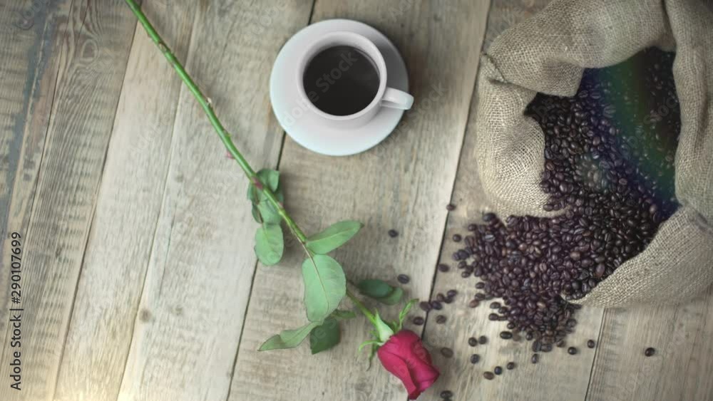 Overhead flat lay shot of a cup of espresso coffee on a wooden table near a bag of jute full of coffee beans. A red rose next to it for a romantic breakfast or break on St. Valentine's day. Overhead flat lay shot of a cup of espresso coffee on a wooden table near a bag of jute full of coffee beans. A red rose next to it for a romantic breakfast or break on St. Valentine's day.